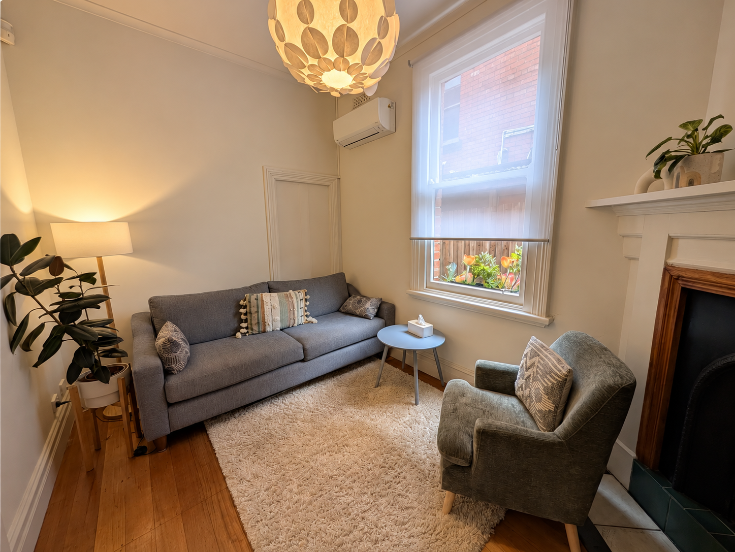 A Camberwell consulting room with a grey sofa, green armchair, heritage fireplace and warm pendant light