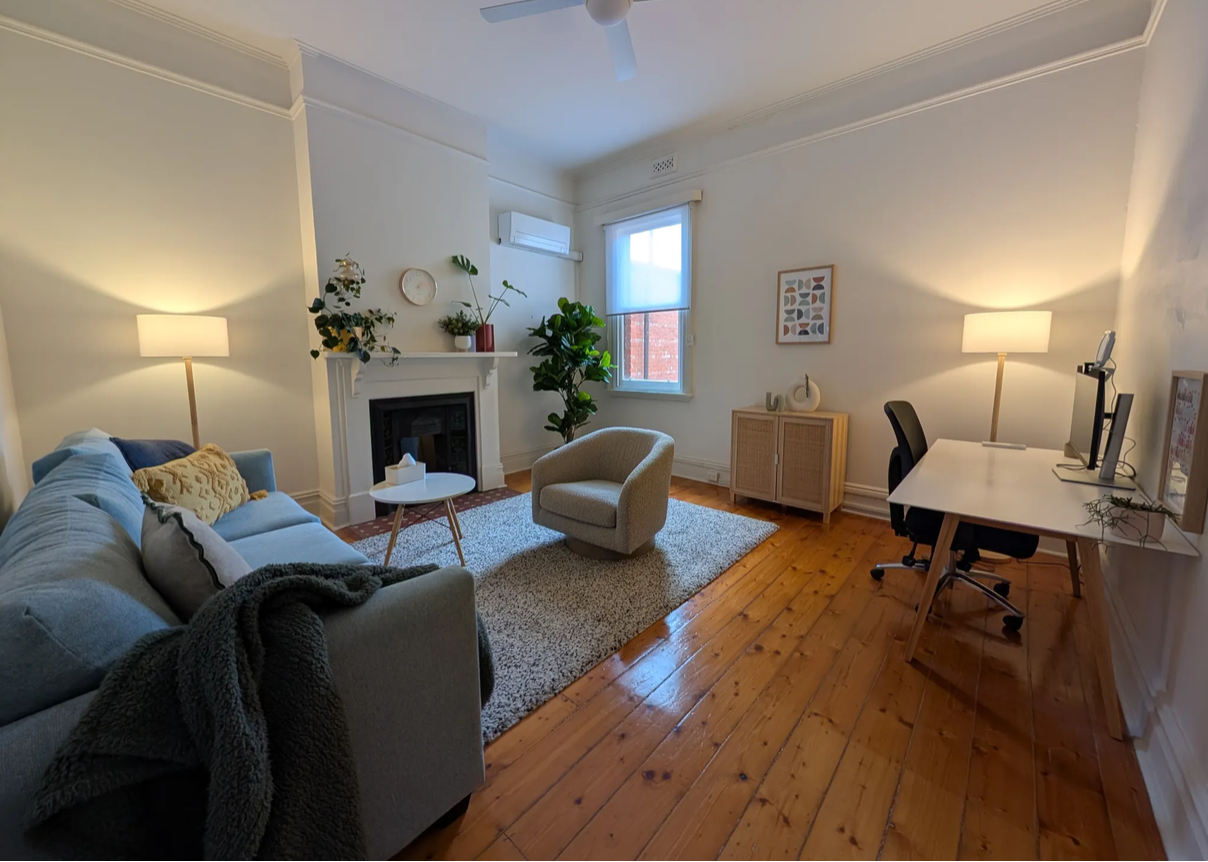 A consulting room at The Camberwell Collective, with a blue sofa, heritage fireplace and upholstered armchair