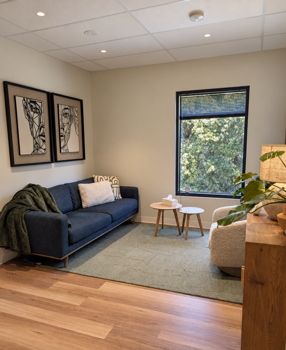 A Hawthorn Hub consulting room with a blue sofa, framed artwork and a leafy window outlook