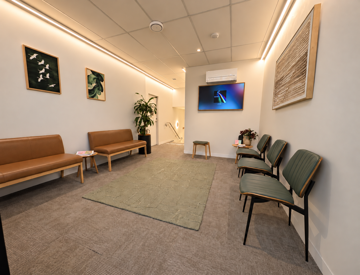 Hawthorn Hub waiting area with tan benches, green chairs, artwork, plants and soft wall lighting